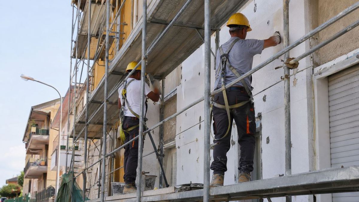 Operai su ponteggio applicano pannelli isolanti a cappotto su facciata condominiale